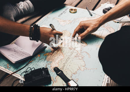Nahaufnahme von Mann und Frau zeigt auf Orte auf der Weltkarte. Frau erwähnenswert Urlaubsplan in einem Tagebuch fest. Stockfoto