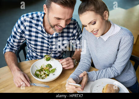 Von oben Schuss von Erwachsenen Mann und Frau am Essentisch Smartphone-Bildschirm schauen und Lächeln Stockfoto