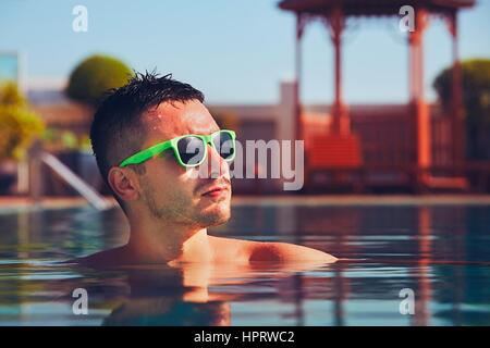 Junger Mann mit Sonnenbrille ruht in den Pool an einem Sommertag. Stockfoto