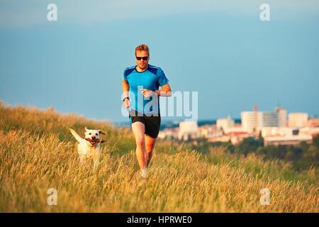 Sport-Lifestyle mit Hund. Sportlicher junger Mann und Labrador Retriever laufen auf dem Hügel außerhalb der Stadt. Prag, Tschechische Republik. Stockfoto