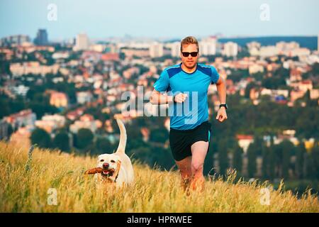 Sport-Lifestyle mit Hund. Sportlicher junger Mann und Labrador Retriever laufen auf dem Hügel außerhalb der Stadt. Prag, Tschechische Republik. Stockfoto