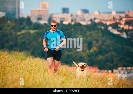 Sport-Lifestyle mit Hund. Sportlicher junger Mann und Labrador Retriever laufen auf dem Hügel außerhalb der Stadt. Prag, Tschechische Republik. Stockfoto