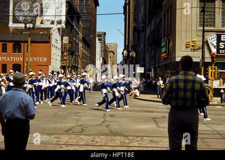 Ein Drill Team bestehend aus Kindern in blauen und weißen Uniformen marschiert nach unten Locust Street während einer Memorial Day Parade in der Innenstadt von St. Louis, Missouri als zwei Männer, von hinten, Blick, 28. Mai 1956. Gebäude einschließlich Avis ein Auto mieten, das katholische Information Center, die Farm und Hause Einsparungen und Loan Association Building, und Scruggs Vandervoort Barney Anhang (jetzt auf dem National Register of Historic Places). Stockfoto