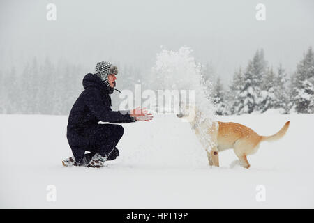 Mann spielt mit seinem gelben Labrador Retriever in Winterlandschaft Stockfoto