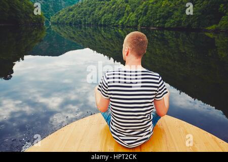 Urlaubsreise auf dem Fluss. Gut aussehender Mann sitzt auf dem Bug des Bootes. Stockfoto