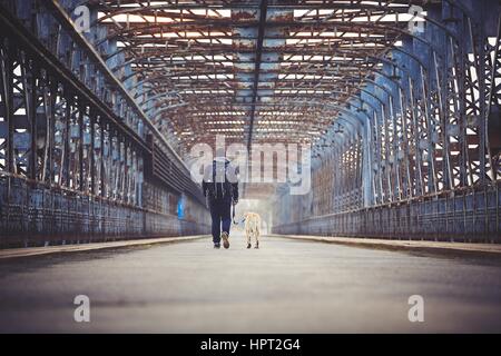 Mann geht mit seinem gelben Labrador Retriever auf der alten Brücke Stockfoto