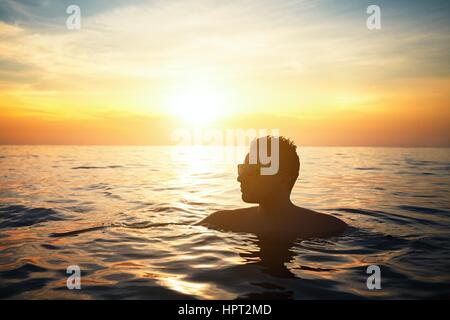 Urlaub am Strand. Junger Mann im Meer bei Sonnenuntergang entspannen. Stockfoto