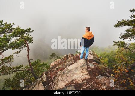 Herbstmorgen. Reisende (Wanderer) oben auf Felsen über dem Flusstal mit dichtem Nebel. Stockfoto