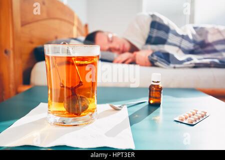 Kranker Mann liegt im Bett unter der Decke. Selektiven Fokus auf den heißen Tee und Medizin auf dem Tisch. Stockfoto