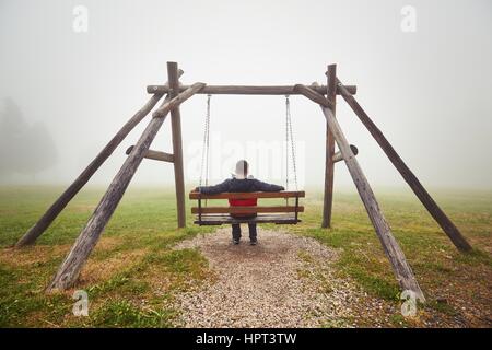 Trauriger Mann auf der Schaukel in geheimnisvollen Nebel Stockfoto