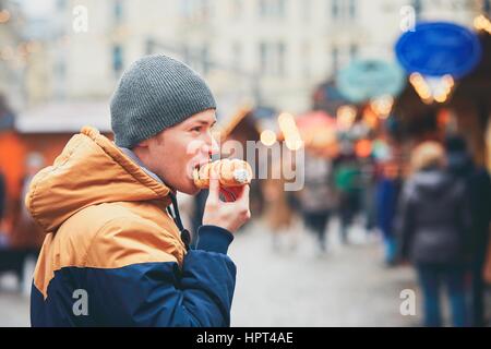 Junger Mann Essen Blätterteig Rollen mit Sahne auf Weihnachtsmarkt, Wien, Österreich Stockfoto