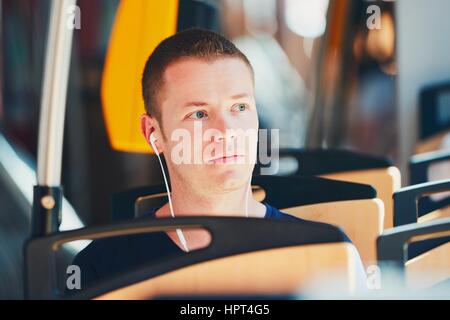 Alltag und pendeln zur Arbeit mit öffentlichen Verkehrsmitteln. Hübscher junger Mann ist mit der Straßenbahn unterwegs. Mann trägt Kopfhörer und Musi hören Stockfoto