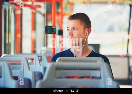 Trauriger junger Mann reist mit der Straßenbahn (Bus). Alltag und pendeln zur Arbeit mit öffentlichen Verkehrsmitteln. Mann trägt Kopfhörer und anhören von mus Stockfoto