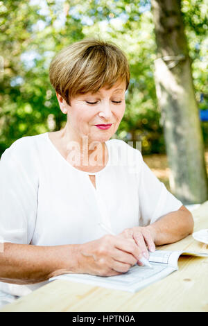 Ältere Frau tun einen Kreuzworträtsel im freien Stockfoto