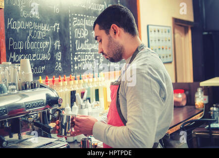 Barista Peitschen Milch für Espresso an der Kaffeemaschine in einem gemütlichen Café. Stockfoto