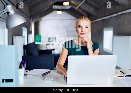 Schöne junge Frau sitzt am Tisch in modernen Coworking Büro Stockfoto
