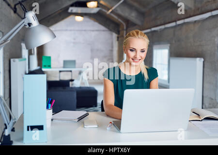 junge Frau lächelt und tippen auf Laptop im modernen Büro Stockfoto