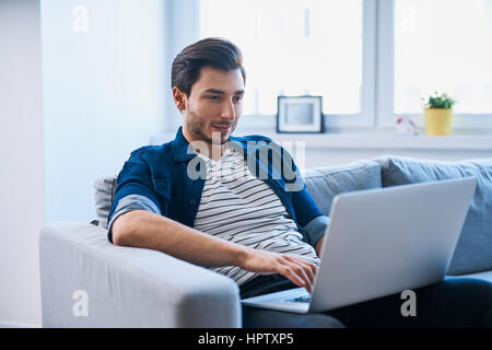 Gut aussehender Mann mit Laptop sitzen entspannt auf sofa Stockfoto