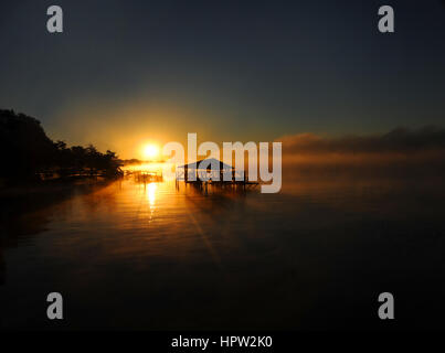 Lake Chicot erstrahlt in goldenen Sonnenaufgang.  Pier und Boot Haus sind Silhouette gegen den frühen Morgen goldene Sonnenstrahlen. Stockfoto