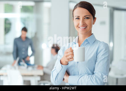 Glücklich zuversichtlich Geschäftsfrau mit einer Kaffeepause und hält einen Becher Büroangestellte auf Hintergrund Stockfoto