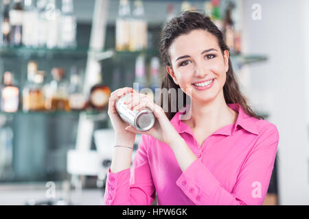 Schöne junge Barista bereitet einen Cocktail mit einem Boston-Shaker und lächelt in die Kamera Stockfoto