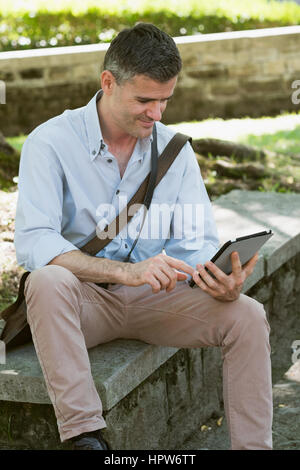 Mann im Park auf einer Bank sitzend und mit einer digitalen Touch-Screen-Tablette, Rasen auf dem Hintergrund Stockfoto