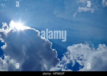 Strahlende Sonne hinter einige weiße Wolken am blauen Himmel Stockfoto