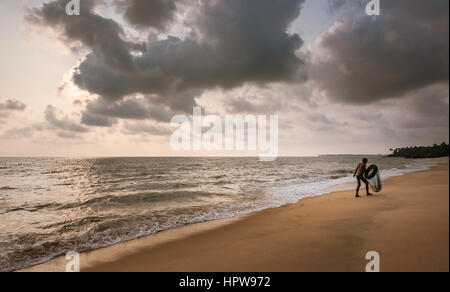 Ein Taucher für Weichtiere ergibt sich aus dem Meer mit seinen Reifen Schwimmer und Net entlang des Strandes mit Blick auf Arabische Meer bei Sonnenuntergang in der Nähe von Kannur, Kerala, Indien. Stockfoto