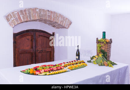 Zusammensetzung der Früchte und geschliffenem Glas Korbflasche beschichtet für Wein Wicker. Auf einem Tisch, beladen mit einem Restaurant, mit Trauben, Feigen, Kaktusfeigen und Blätter. A Stockfoto