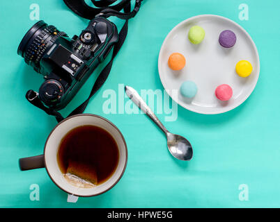 bunte französische Macaron, Tasse Tee und SLR-Kamera auf grünem Hintergrund-Draufsicht Stockfoto