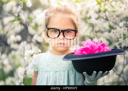 Lustiges Mädchen Brille und Handschuhen und mit Hut im Frühlingsgarten spielen. Stockfoto