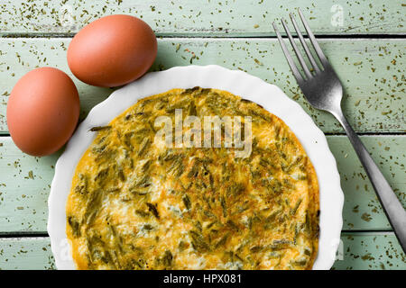 eine spanische Tortilla de Espárragos, ein Omelett mit grünem Spargel und einigen Eiern auf einem blassen Grün rustikalen Holztisch gemacht Stockfoto