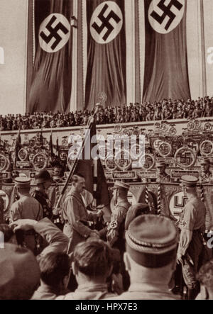 Adolf Hitler im Jahr 1934 am Reichsparteitag (nationalen Parteitag) Händeschütteln w / Soldat auf Stein Terrasse von Hall of Honor unter Hakenkreuz-Fahnen. Stockfoto