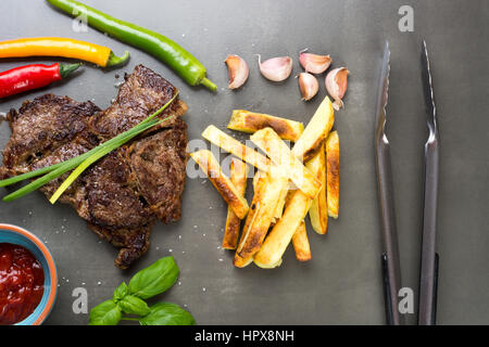 Gut gemacht Rindersteak mit Chips auf dunklen Schiefer Teller Stockfoto