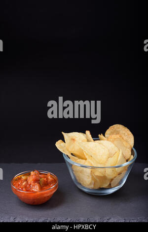 Knusprige Pommes Frites mit Meersalz in Glas Schüssel, Tomatensauce, Steinplatte, schwarzer Hintergrund, Platz für Text. Stockfoto
