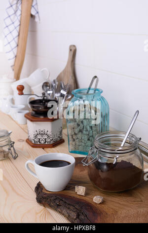 Gemahlener Kaffee mischen und frisch gebrühter Kaffee in eine weiße Tasse mit Rohrzucker. Hölzerne Buffet Zähler voller Utensil. Hellen Hintergrund. Stockfoto