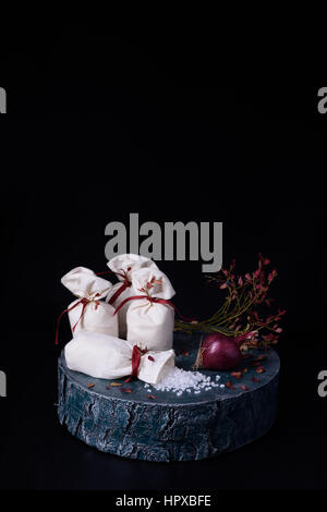 Vintage Stillleben mit Meersalz in Stofftaschen mit Blaackberry Zweigen und roten Zwiebeln auf einem Baumstamm. Schwarzen Sie Hintergrund, kopieren Sie Raum zu. Stockfoto