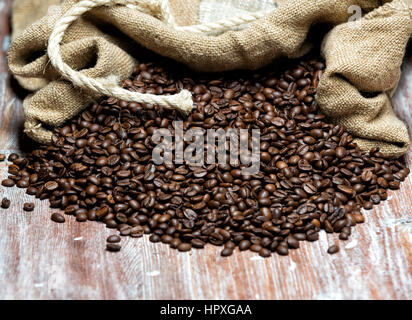 geröstete Kaffeebohnen aus der Tasche auf einem Holztisch verschüttet Stockfoto