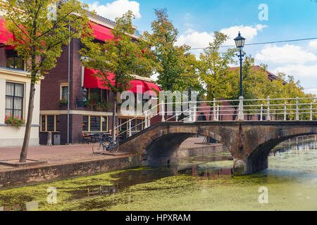 Die malerische Brücke mit einer Laterne durch den Kanal und typische Häuser an einem sonnigen Tag in Delft, Zuid-Holland, Niederlande. Stockfoto