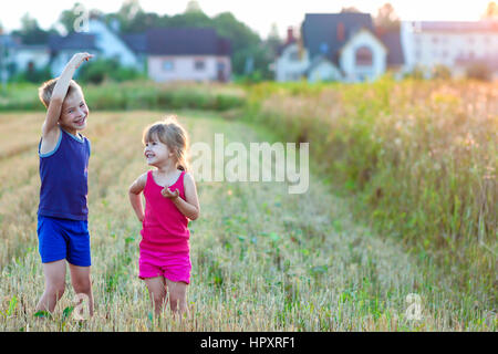 Zwei glückliche frohe frohe Kinder Jungen und Mädchen Bruder und Schwester im Weizenfeld mit unscharfen Häuser im Hintergrund stehen und Spaß Stockfoto