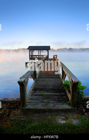 Holzsteg führt über ruhige Gewässer des frühen Morgens am See Chicot Lake Village, Arkansas andocken.  Dock ist verwittert und Sonnenstrahlen färben es gehen Stockfoto