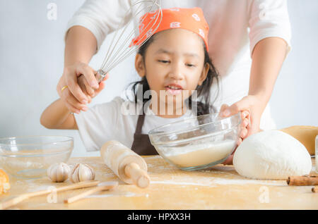 Schuss, die kleine Asiatin mit Edelstahl Schneebesen und Bäckerei Teig Mehl im Glas Schüssel und Mutter Hände, Fokus auf die geringe Schärfentiefe f Hände hautnah Stockfoto