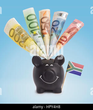 Zehn, zwanzig, fünfzig, hundert und ein 200 Euro-Banknote in ein lächelndes Sparschwein in Südafrika. (Serie) Stockfoto