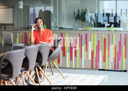 Voller Körper-Bild von einer attraktiven jungen afroamerikanischen Frau sitzend auf einem schönen braunen Stuhl am Ende einen Konferenztisch in der Business-Dur Stockfoto