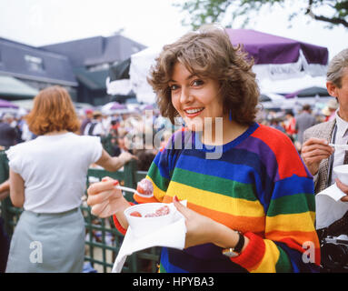 Junge Frau essen Erdbeeren mit Sahne an den Meisterschaften, Wimbledon, London Borough von Merton, Greater London, England, Vereinigtes Königreich Stockfoto