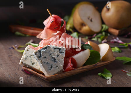 Blauschimmelkäse mit Prosciutto und Birne auf einem alten Holztisch Stockfoto