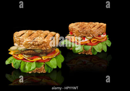 Zwei Sandwiches mit verschiedenen Füllungen auf einem schwarzen Hintergrund mit einem Schnitzel, Käse, Tomaten, Schinken, Gurken und Kräuter. Stockfoto