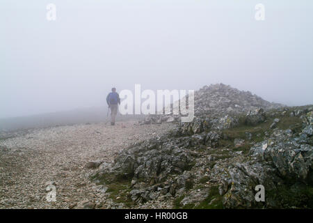 Einsamer Wanderer im Nebel auf steinigen Bergweg durch große Cairn in der Nähe von Scafell Pike im englischen Lake district Stockfoto