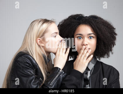 Zwei Teenager Hipster Mädchen im Studio. Man sagt dem anderen etwas schreckliches Geheimnis. Isoliert auf weißem Hintergrund. Stockfoto