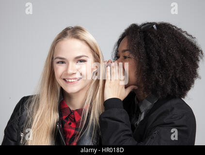 Zwei Teenager Hipster Mädchen im Studio. Man sagt dem anderen etwas schreckliches Geheimnis. Isoliert auf weißem Hintergrund. Stockfoto